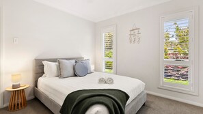 Une chambre à coucher avec un lit, une lampe de chevet et deux fenêtres équipées de stores.