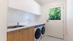 Une petite buanderie équipée d’un évier, de meubles en bois et d’un lave-linge.