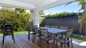An outdoor patio with a table and chairs, a barbecue grill, and a view of a backyard with a fence and trees. - Culburra Cove - Pet Friendly - 5 Mins Walk to the Beach (Culburra Beach)