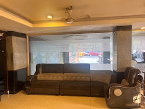 A modern living area with a sofa, a massage chair, and a ceiling fan. - Hotel golden way  (Vijayawada)