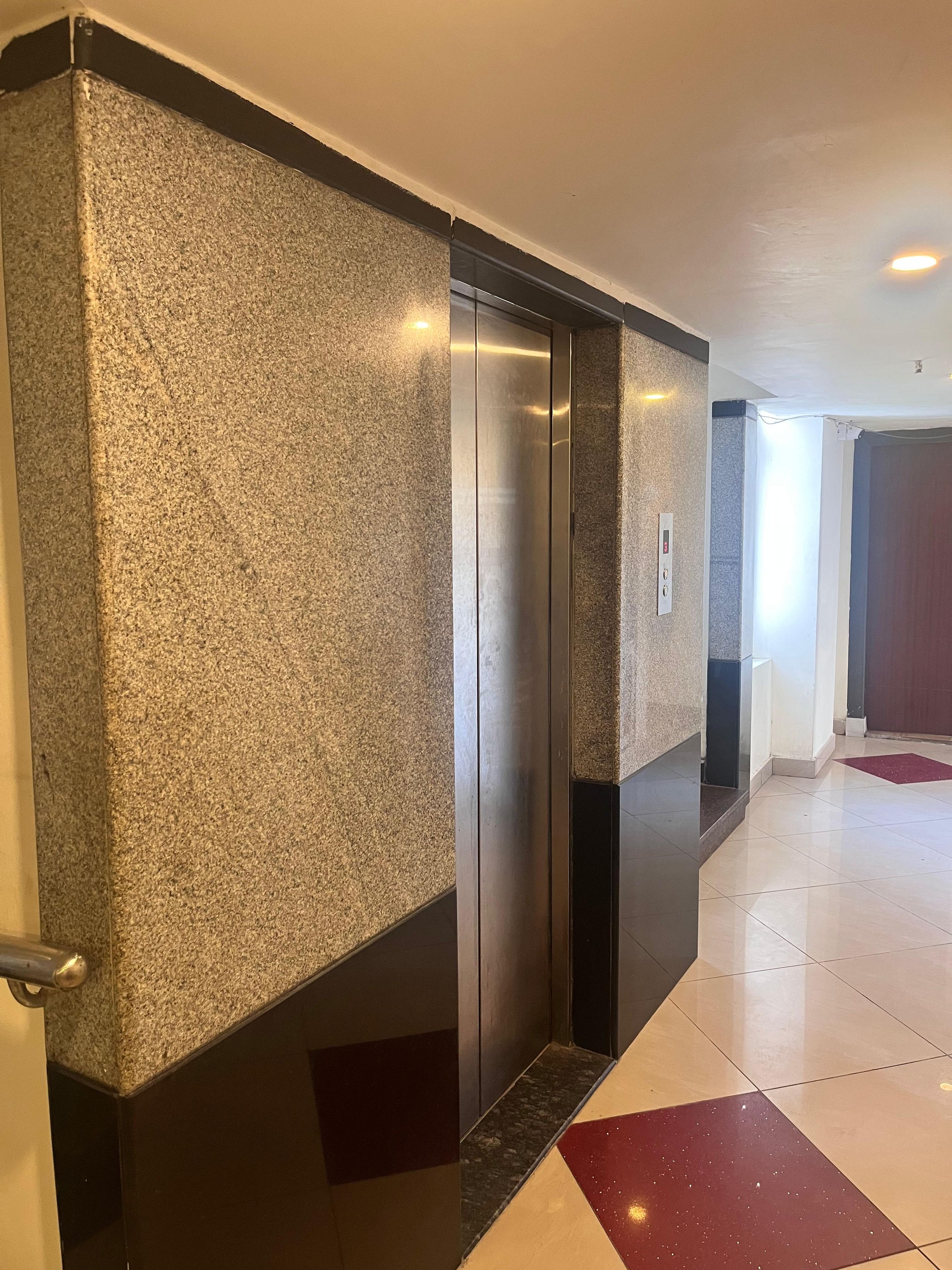 A hallway with a textured wall, an elevator, a red carpet, and a door.