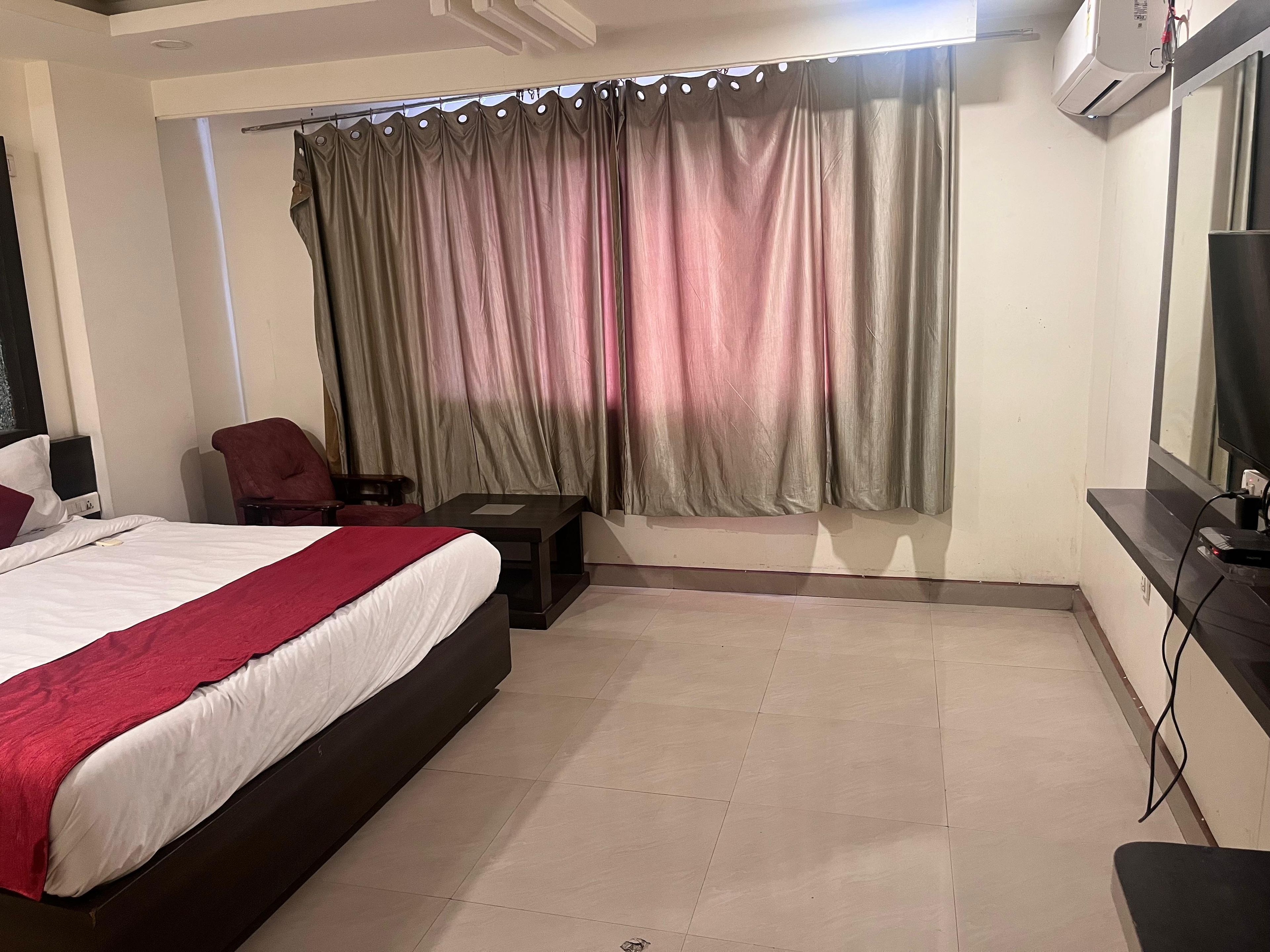 A hotel room with a bed, a desk, a chair, a TV, and a window with curtains.