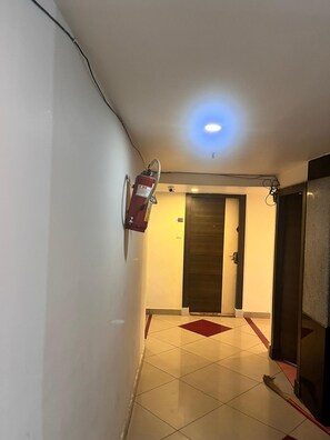 Un pasillo con un extintor fijado a la pared, una puerta al final y suelo de baldosas.