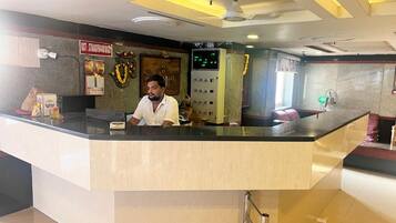 A reception desk with a man seated behind it, a control panel, and a wall-mounted sign.