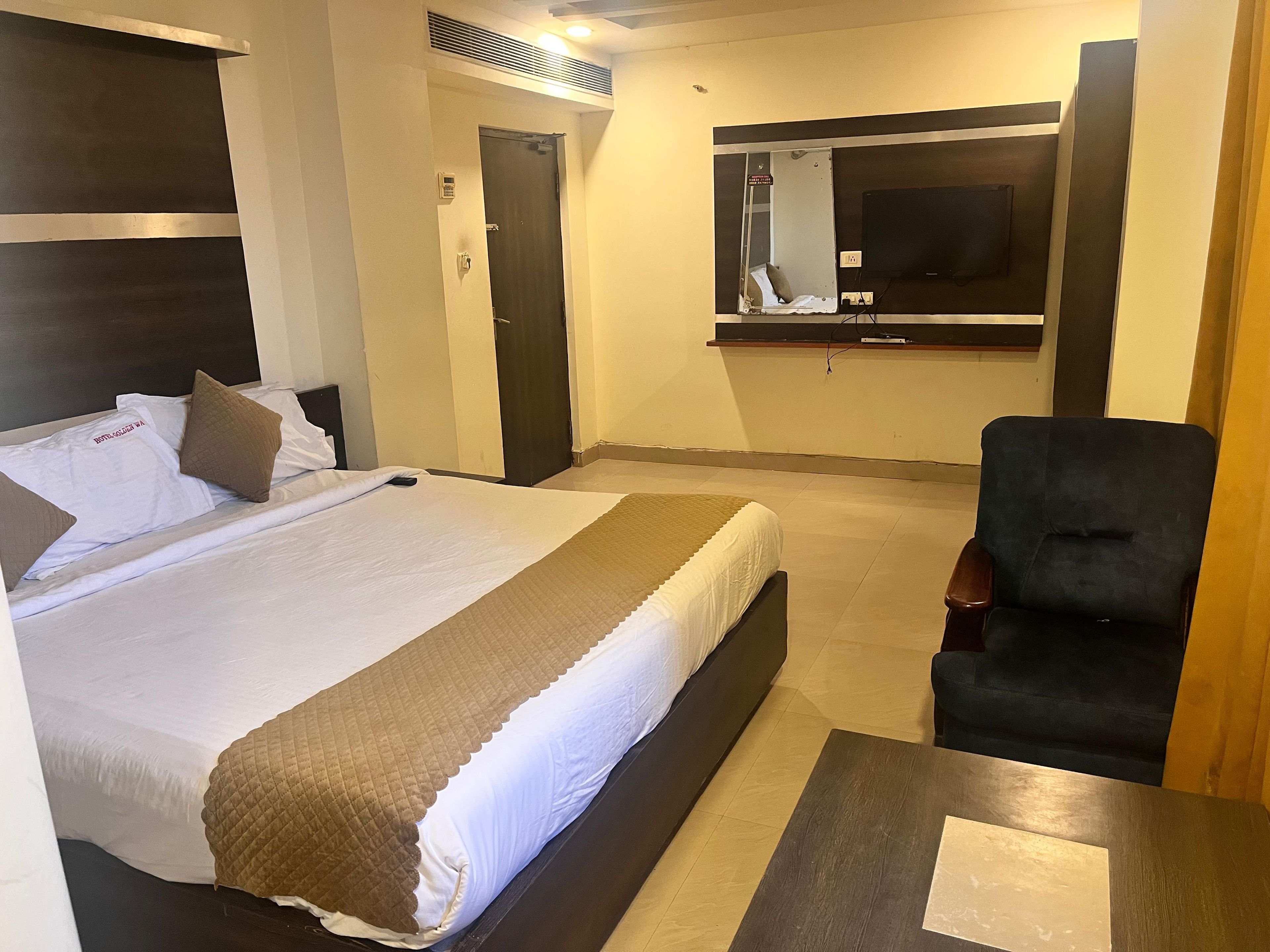 A hotel room with a bed, a desk, a chair, a television, and a door.