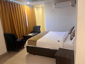 A hotel room with a bed, a desk, a chair, and a curtain. - Hotel golden way  (Vijayawada)