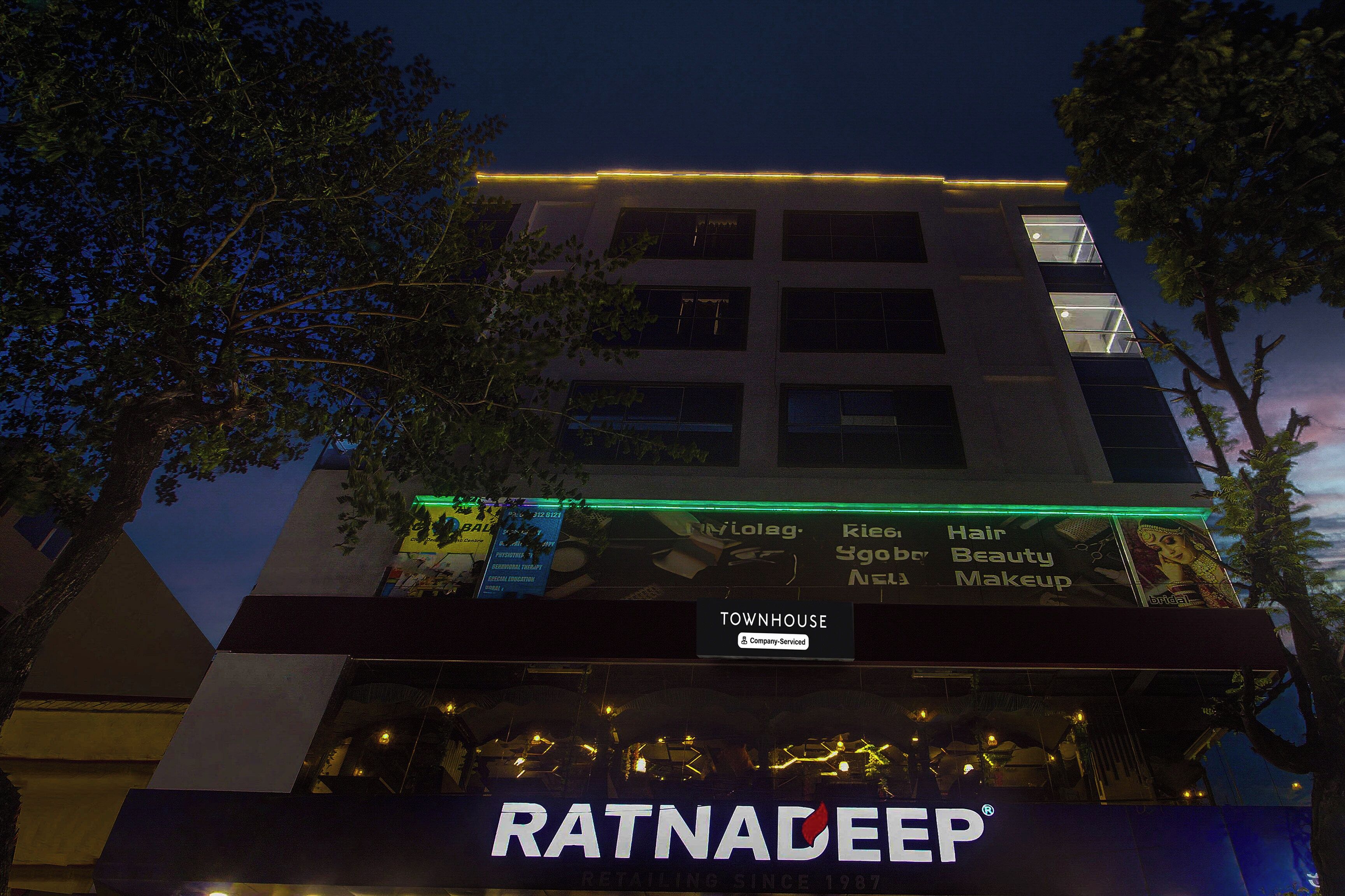 A building with multiple floors, a sign for 'Ratnadeep' at the ground level, and illuminated signage above.
