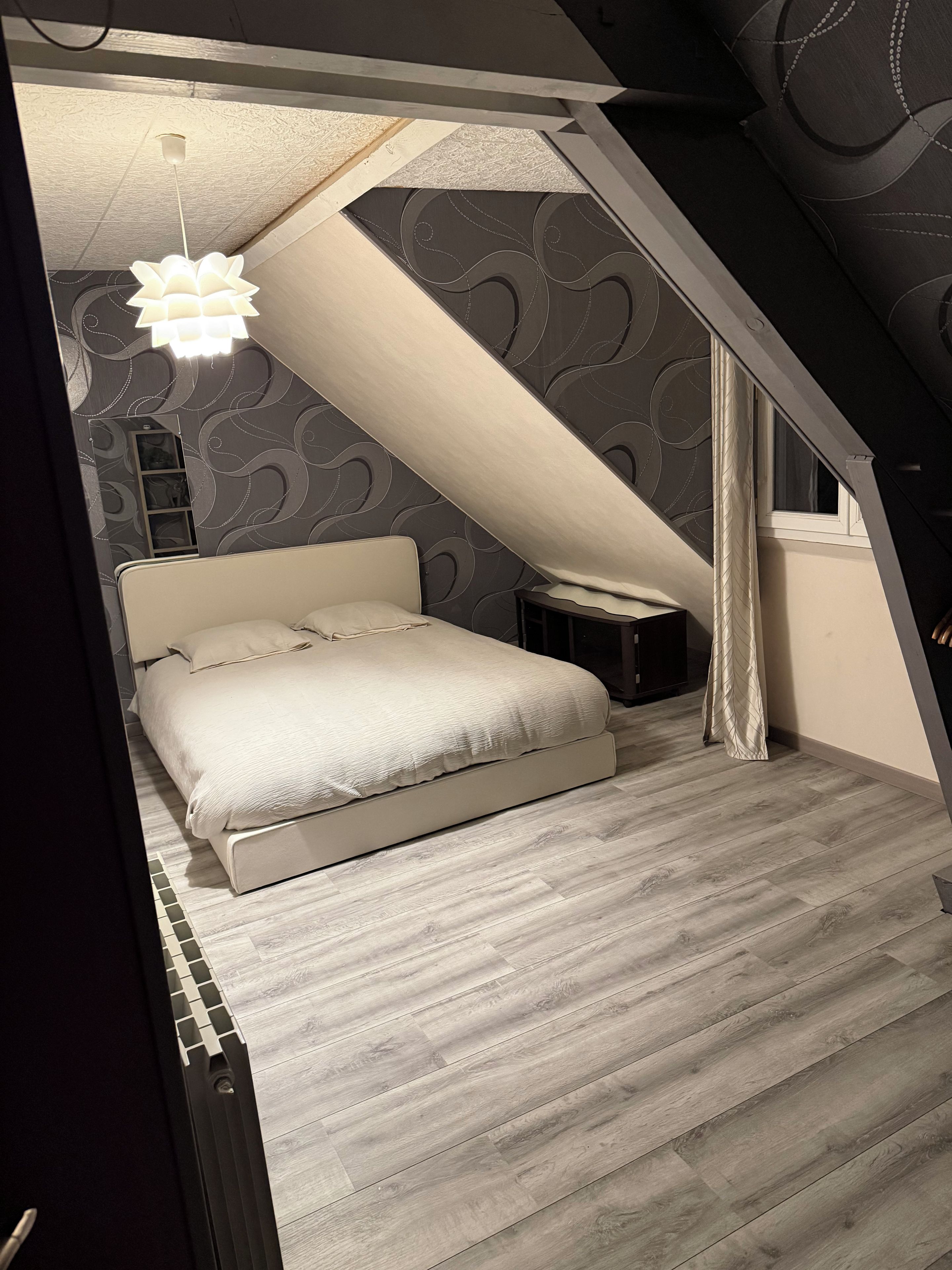 Ein Schlafzimmer mit einem Bett, einem Nachttisch, einer Pendelleuchte und einem Fenster mit Vorhängen.
