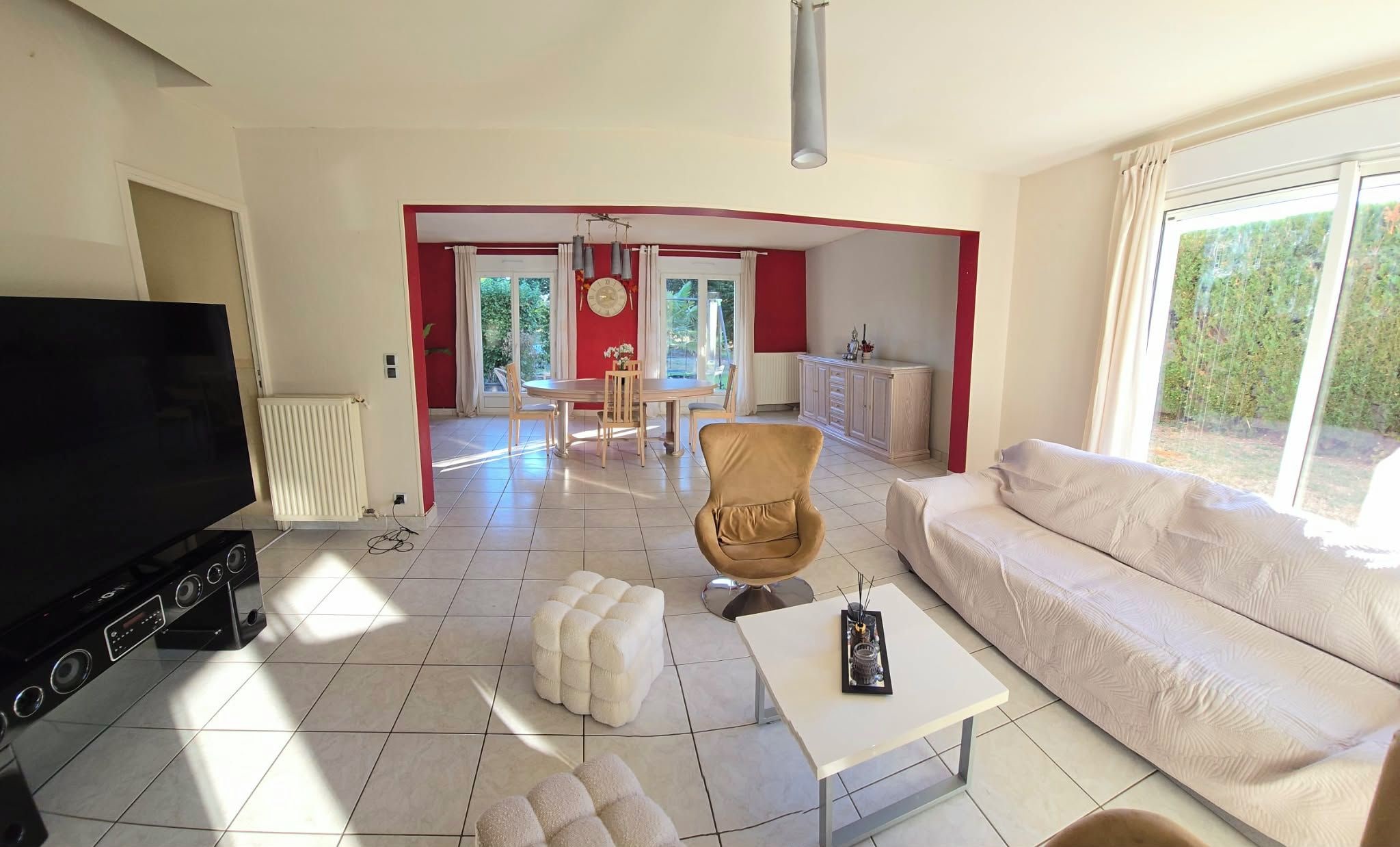 A living room with a TV, sofa, ottoman, and a dining area with chairs and a table.