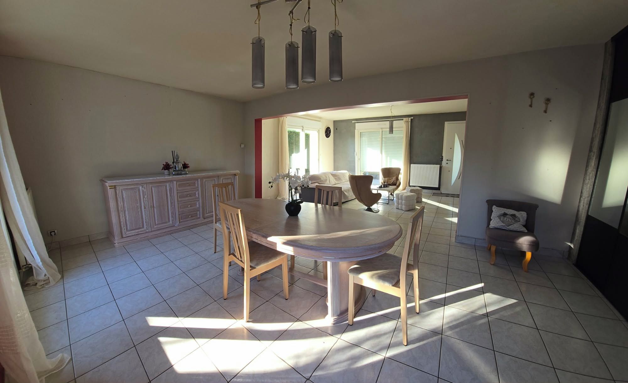 A spacious dining area with a round table and chairs, a kitchen with a cabinet, and a living area with a sofa and armchair.