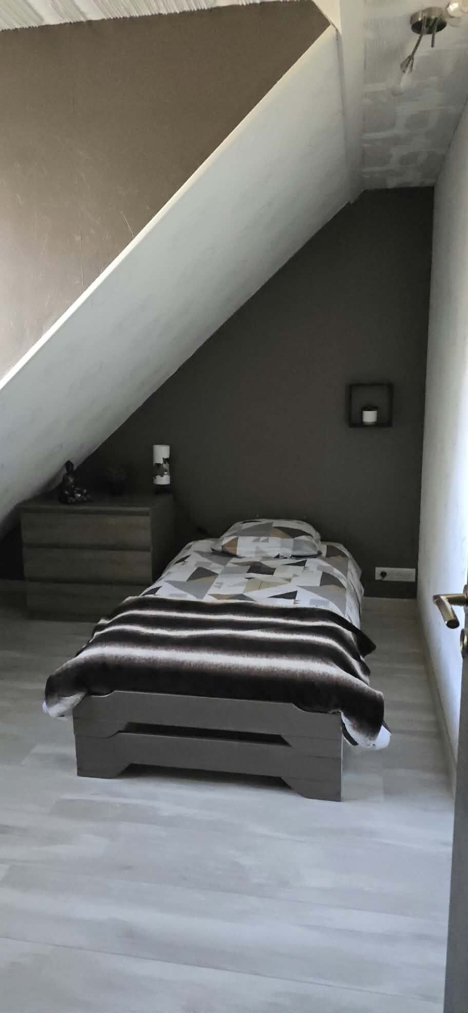 Quarto com cama, mesa de cabeceira, abajur e tomada na parede.