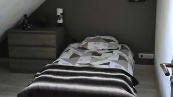 Quarto com cama, mesa de cabeceira, abajur e tomada na parede.