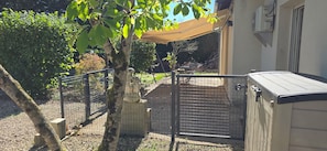 Zona exterior tancada amb una tanca metàl·lica, un arbre i un edifici amb teulada inclinada.