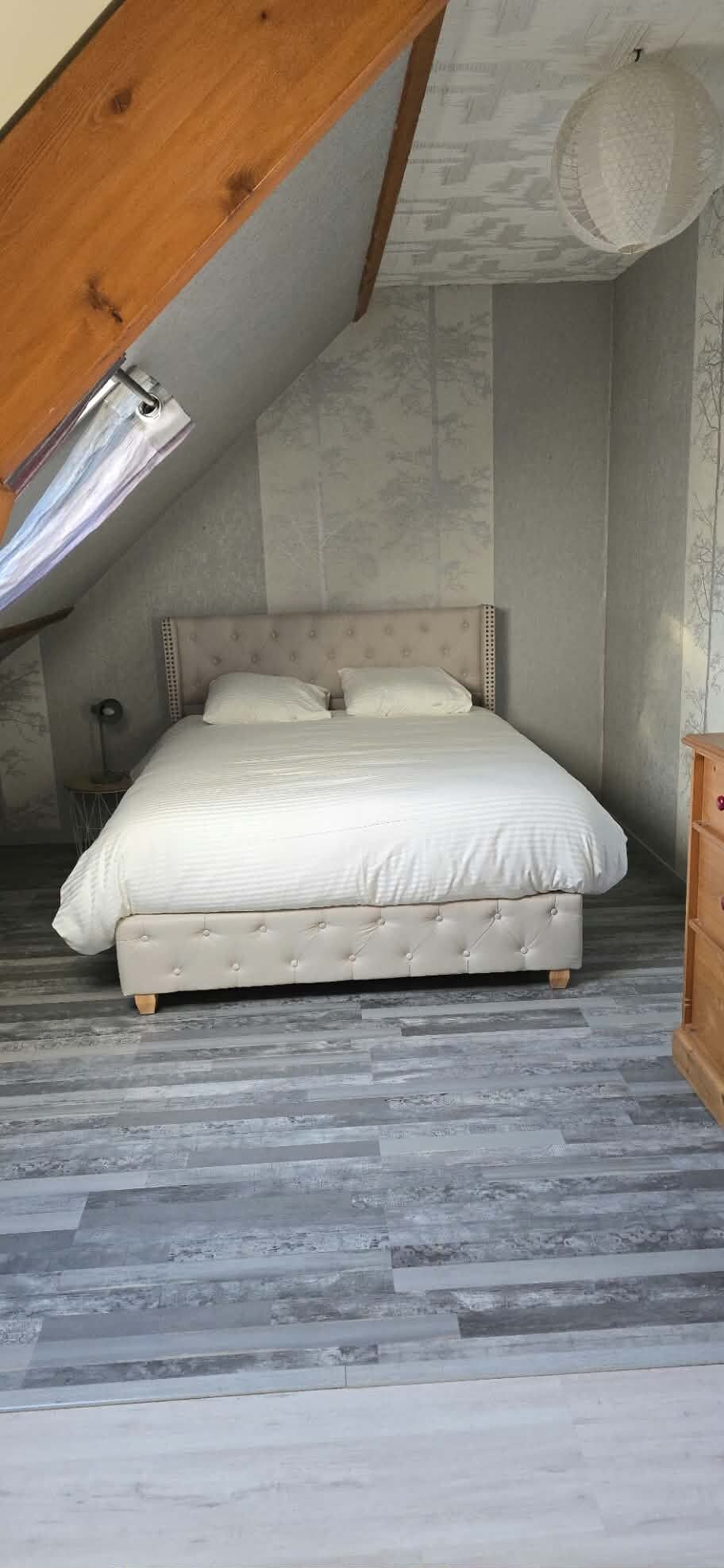 Ein Schlafzimmer mit Schräge, einem Bett mit einer Knopfleiste und Holzdielenboden.