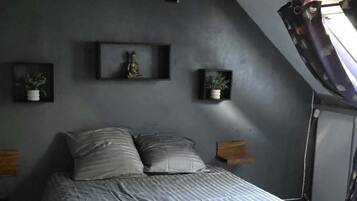 A bedroom with a sloped ceiling, a bed with a grey bedspread, two bedside tables with lamps, and wall-mounted shelves with decorative items.