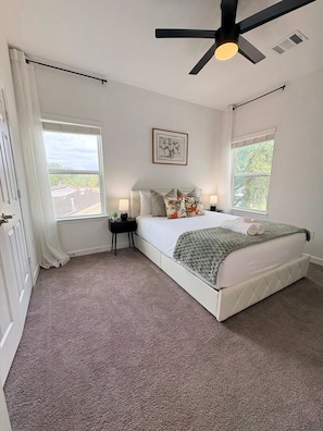Quarto com cama, duas mesas de cabeceira, um ventilador de teto e duas janelas.