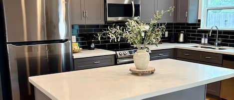 Une cuisine moderne dotée d’un îlot central, d’appareils électroménagers en acier inoxydable et de meubles de rangement aux couleurs sombres.