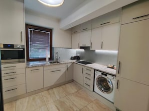 A modern kitchen with a built-in oven, a washing machine, and a window with blinds. - Stylish Apartment in Zabłocie (Kraków)