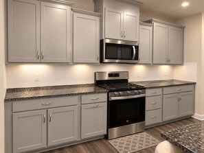 A kitchen with grey cabinets, a stainless steel microwave, a gas stove, and an oven. - Luxury 1BR Retreat Near Uptown, Speedways & UNCC (Charlotte)