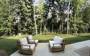 An outdoor seating area with two wooden chairs and a table, surrounded by a well-maintained lawn and a dense tree line. - Luxury 1BR Retreat Near Uptown, Speedways & UNCC (Charlotte)