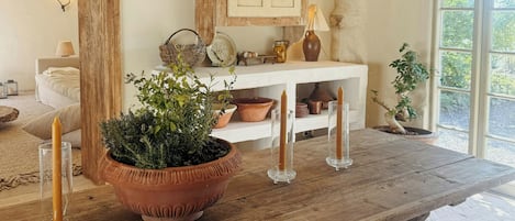 A rustic wooden dining table with candles, a potted plant, and a hanging light fixture in a cozy room with a large mirror and a cabinet.