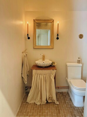 Un baño con un lavamanos blanco, un tocador de madera, un espejo, un perchero para toallas y un inodoro.