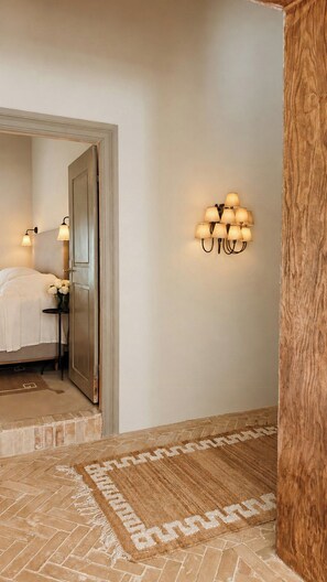 A hotel room with a bed, a nightstand, a lamp, a wall-mounted light fixture, and a patterned rug.