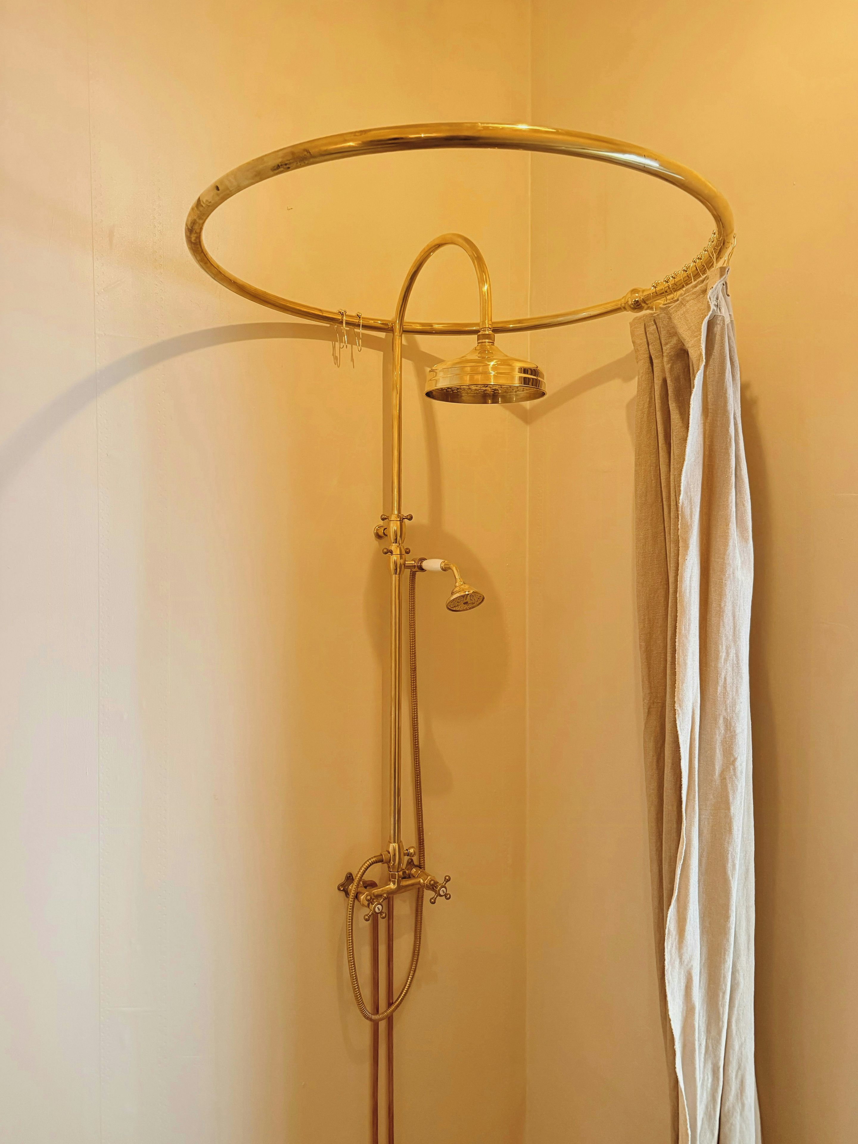 A shower with a gold-colored shower head and control knobs, a glass-enclosed shower head, and a curtain.