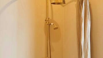 A shower with a gold-colored shower head and control knobs, a glass-enclosed shower head, and a curtain.