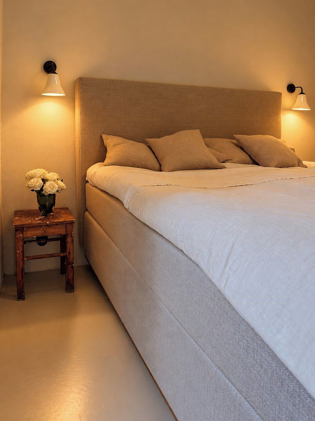 Een slaapkamer met een groot bed, twee bedlampjes en een klein tafeltje met een bloevas.