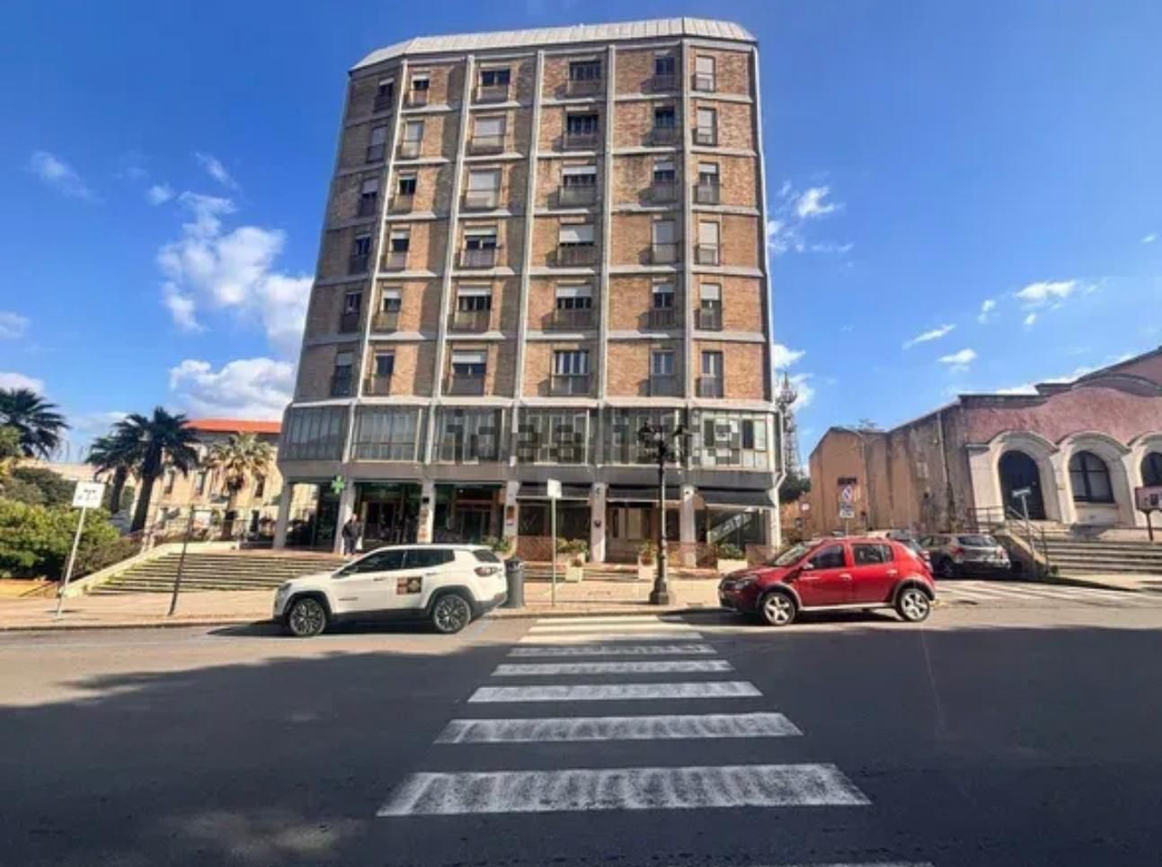 A multi-story building with a ground-level commercial space, a pedestrian crossing, and parked cars.