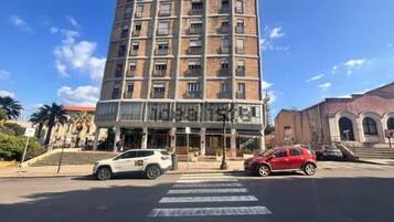 A multi-story building with a ground-level commercial space, a pedestrian crossing, and parked cars.
