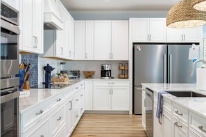 A modern kitchen with white cabinets, stainless steel appliances, and a wooden floor. - Walk to Beach | Hot Tub | 9BR/5BA | Sleeps 20+ (Surf City)
