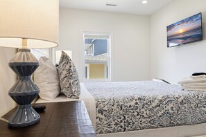 A hotel room with a bed, a lamp, a TV, and a window with a view of a building. - Walk to Beach | Hot Tub | 9BR/5BA | Sleeps 20+ (Surf City)