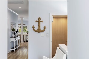 A hallway with a white wall, a wooden door, and a decorative anchor. There is a white console table with a vase and a plant. - Walk to Beach | Hot Tub | 9BR/5BA | Sleeps 20+ (Surf City)