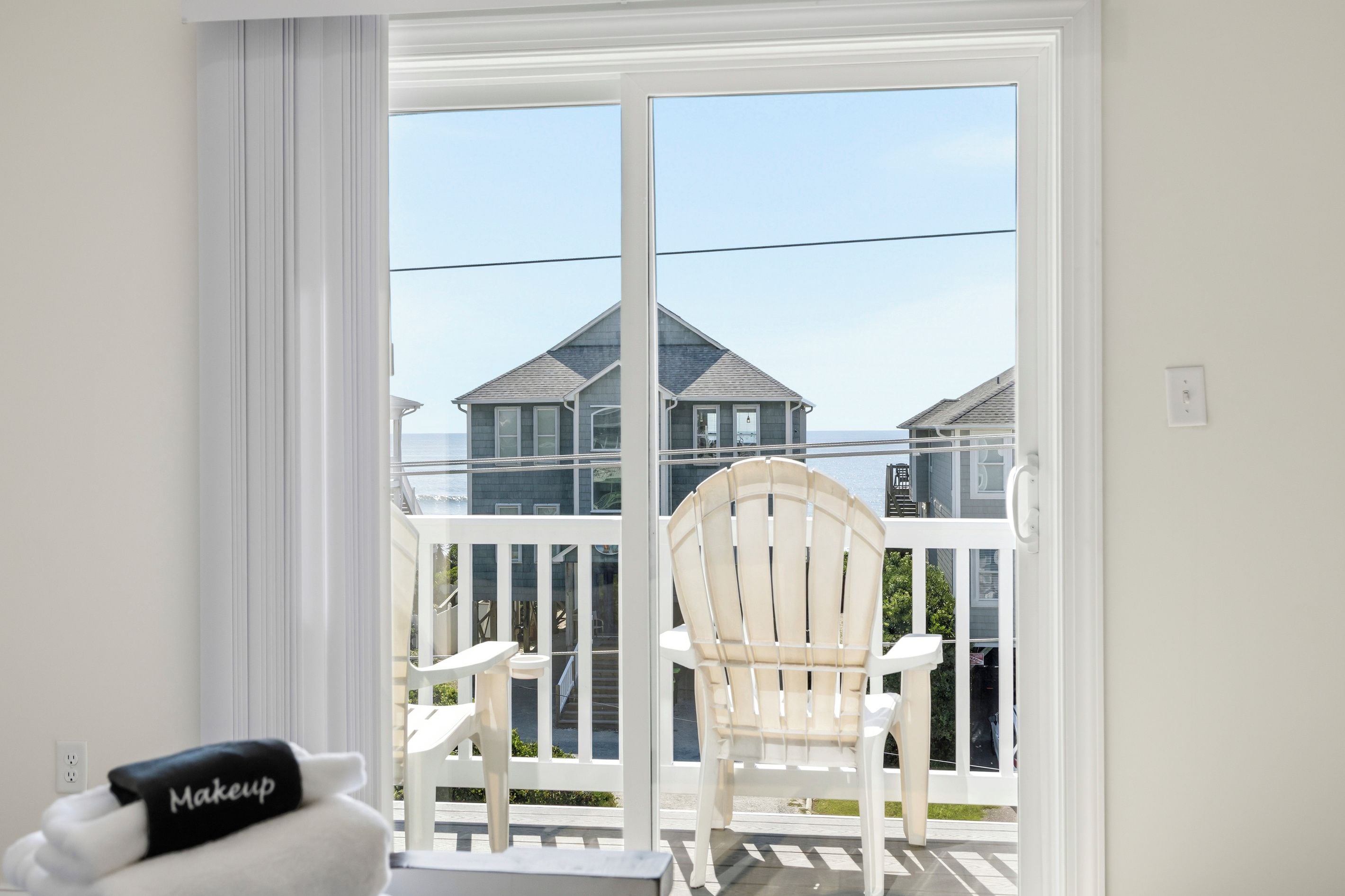 A balcony with a white chair and a small table, overlooking a residential area with houses.
