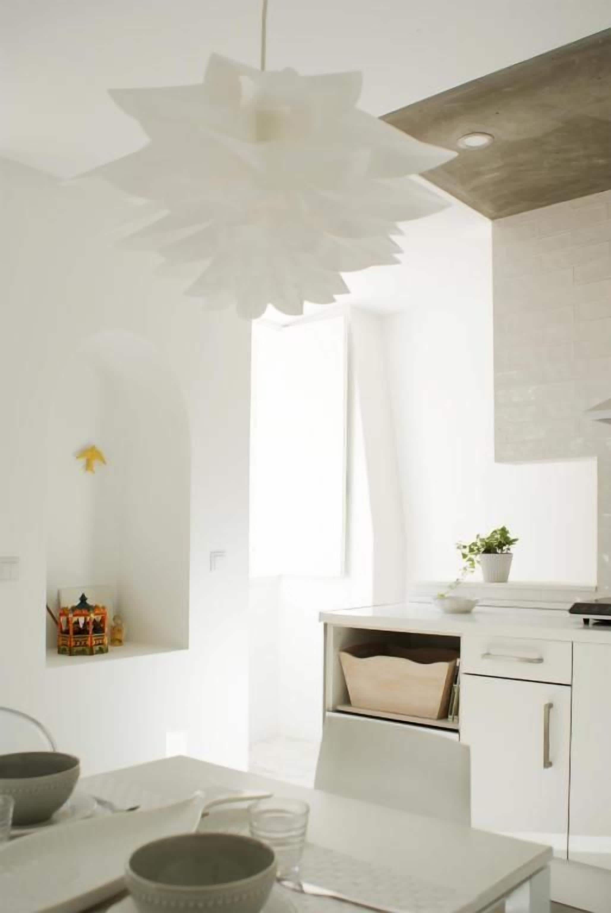 Una cocina moderna con armarios blancos, una lámpara de papel con forma de flor colgante y una pequeña planta en maceta sobre la encimera.