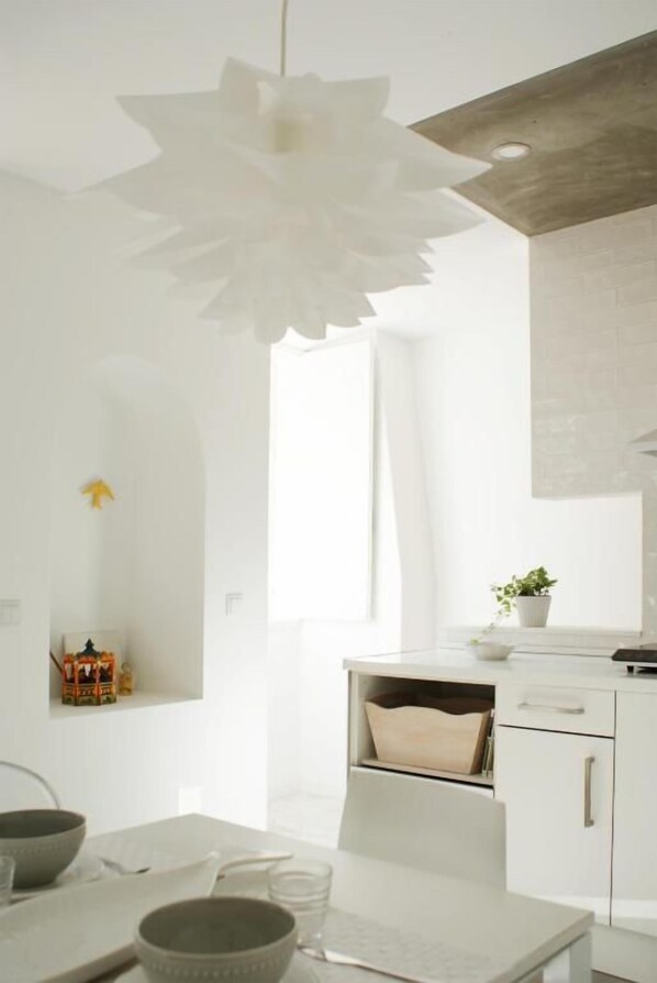 Una cocina moderna con armarios blancos, una lámpara de papel con forma de flor colgante y una pequeña planta en maceta sobre la encimera.