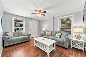 Ein Wohnzimmer mit zwei grauen Sofas, einem weißen Couchtisch und einem Deckenventilator.