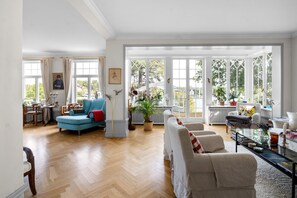 Ein geräumiges Wohnzimmer mit großem Fenster, einem blauen Sessel und einem weißen Sofa.