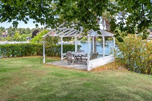 Ein Pavillon mit Glasveranda mit Blick auf ein Gewässer, umgeben von Gras und Bäumen.