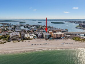 Ein Luftbild einer Küstenstadt mit einem markanten Hotel, das durch einen großen, roten Pfeil hervorgehoben wird. Es liegt in der Nähe eines Strandes und des Wassers.