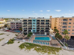 Ein mehrstöckiges Hotel mit Schwimmbad und Liegestühlen direkt am Strand.