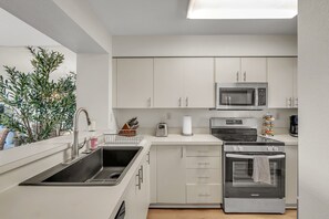 A modern kitchen with stainless steel appliances, white cabinetry, and a built-in oven. - Pool, Hot Tub, Beach Area | Intracoastal Views | Bahia Vista 529 - Bahia Breeze (St. Petersburg)