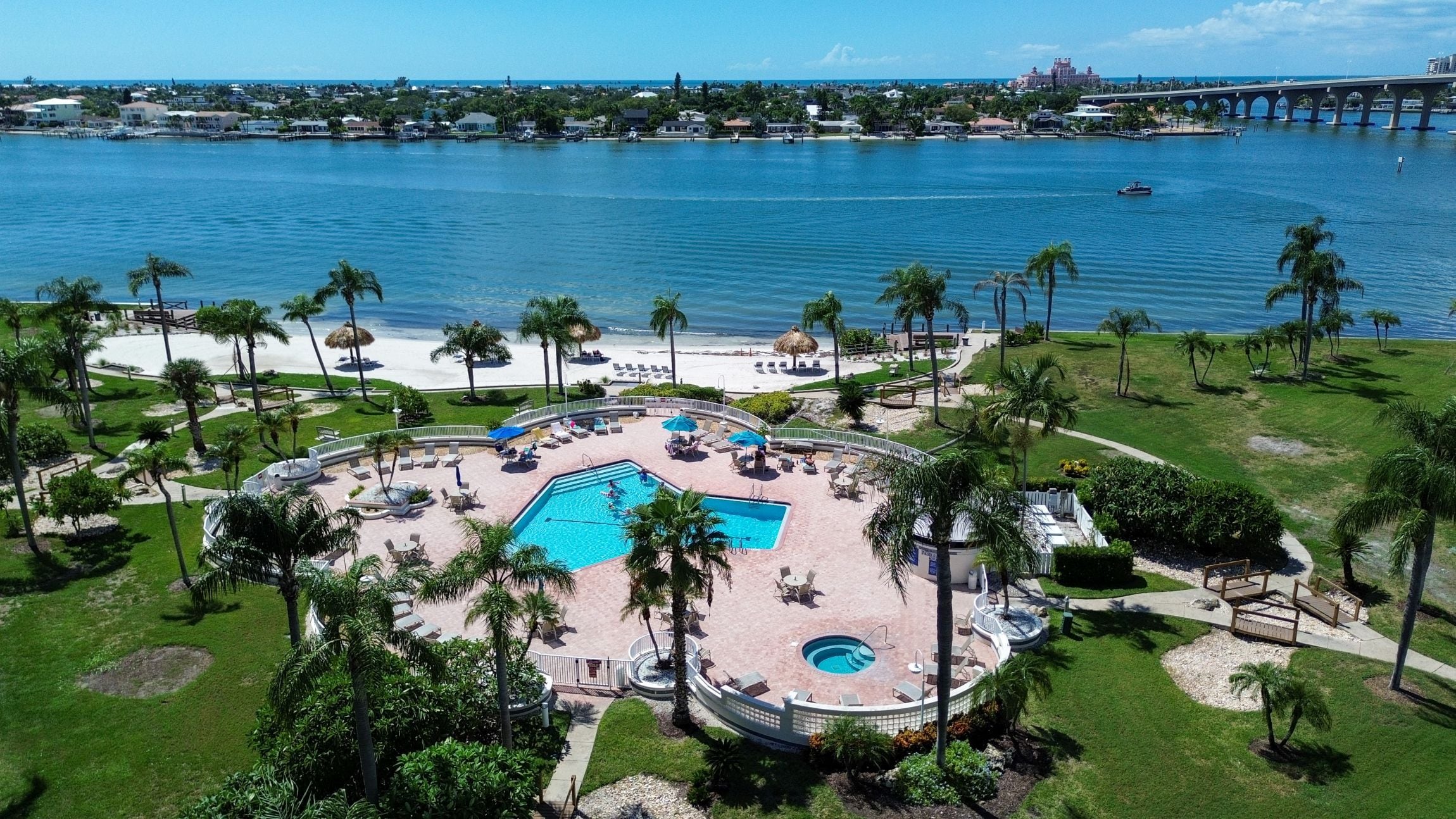 A resort with a central swimming pool, palm trees, and a view of the ocean.