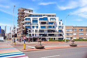 A modern multi-story building with balconies, a pedestrian crossing, and flower planters. - Station Square Stay for 4 (Blankenberge)