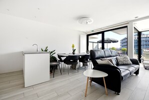 A modern living space with a kitchen, dining area, and a black leather sofa with wooden legs. - Station Square Stay for 4 (Blankenberge)
