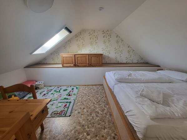 Un dormitorio con techo inclinado, una cama, un armario de madera, una mesita pequeña y una alfombra estampada.