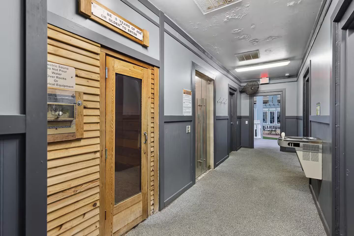 Hallway featuring a wood-paneled sauna entrance, drinking fountain, and exit.