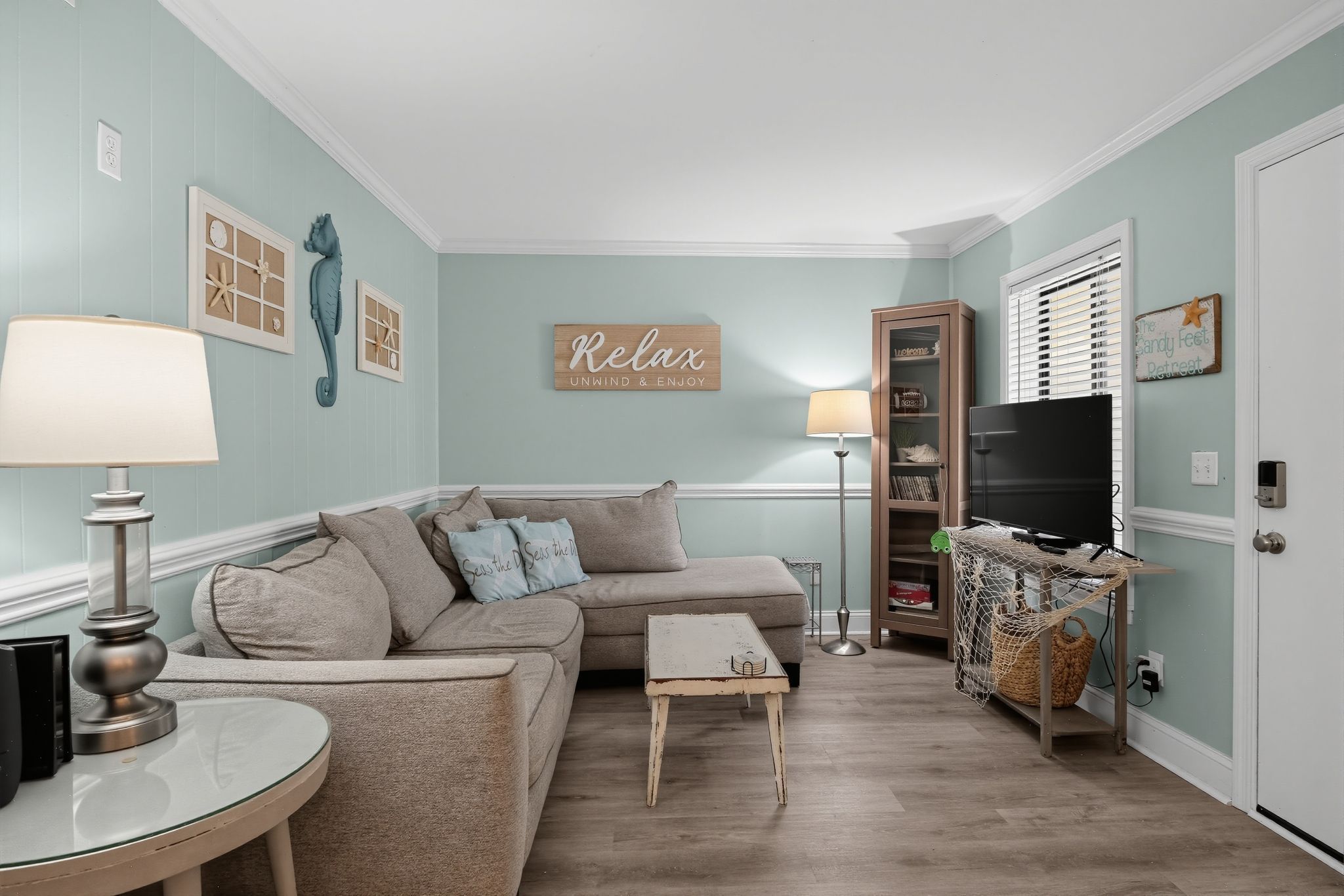 A living room with a beige sofa, a small side table, a lamp, a TV, and a bookshelf.